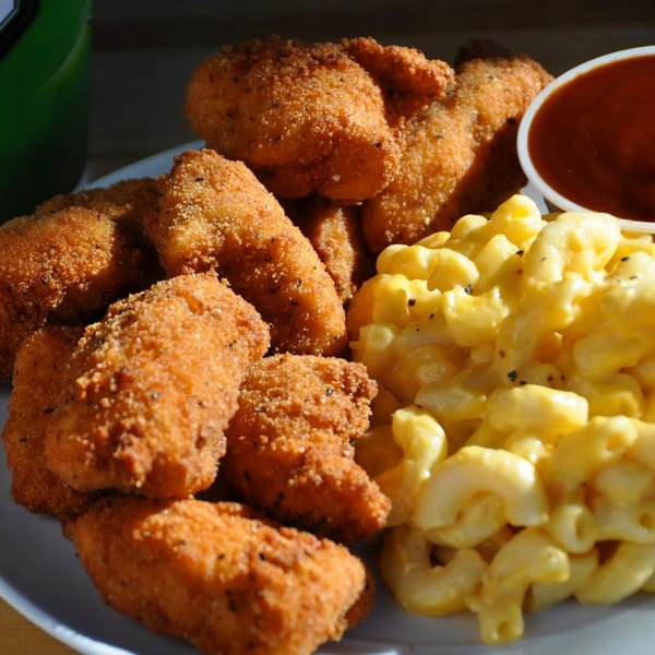 A plate of crispy fried chicken nuggets, creamy macaroni and cheese, and a side of dipping sauce.