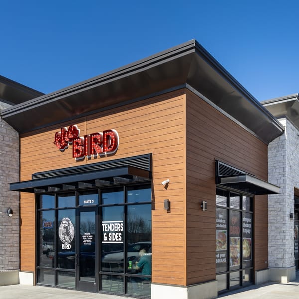 The Bird fried chicken restaurant exterior with wood siding, large windows, and a red neon sign.