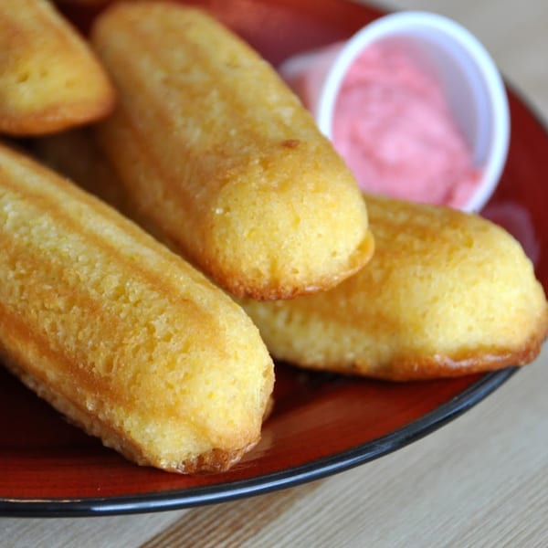 Golden brown corn dog muffins on a red plate with a side of pink dipping sauce.