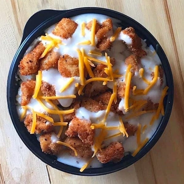 A black bowl filled with The Bird's fried chicken bites, gravy, and shredded cheddar cheese.