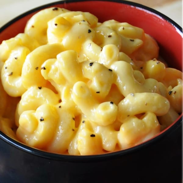 Creamy macaroni and cheese with black pepper in a black bowl with a red rim.