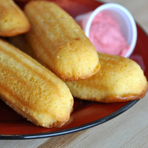 Golden-brown corn dog nuggets on a red plate with a side of pink dipping sauce.